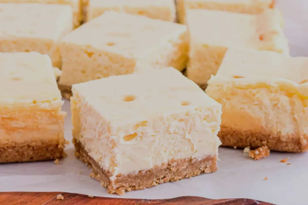 Slices of creamy cheesecake with a graham cracker crust arranged on a white surface.