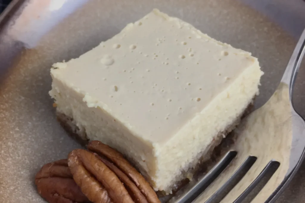 A piece of cheesecake on a plate with pecans beside it.