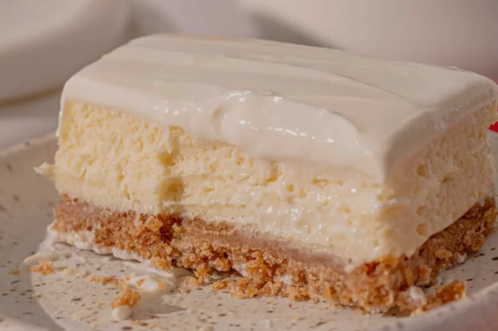 A slice of creamy cheesecake with a graham cracker crust and a smooth frosting on top.