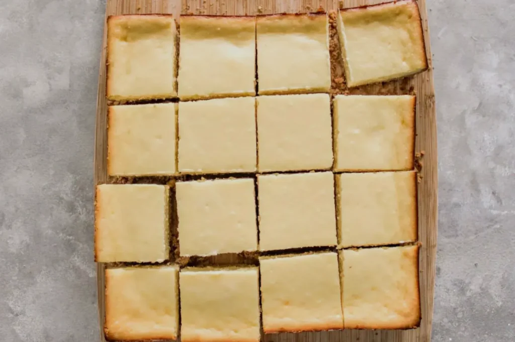 A rectangular pan of cut cheesecake bars arranged in a grid pattern on a wooden board.