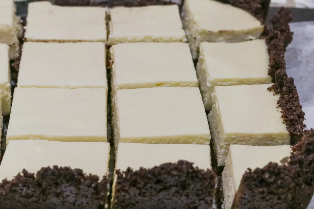 A close-up of a cut cheesecake with a chocolate crust, showing rectangular slices arranged neatly.