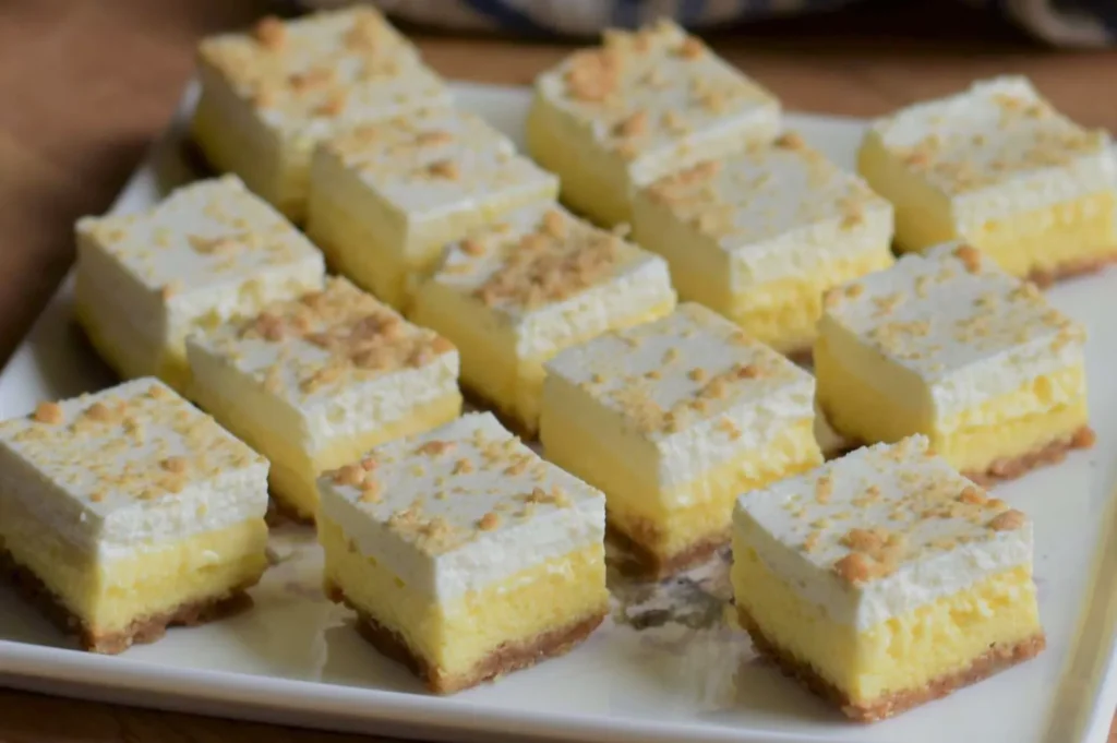 A plate of lemon dessert squares with a creamy layer and a graham cracker crust.