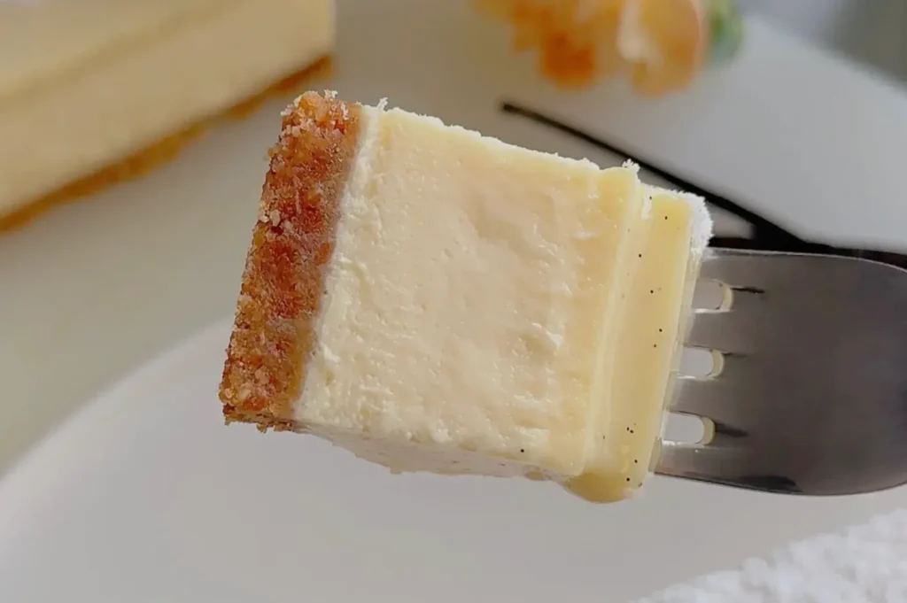A close-up of a fork holding a piece of creamy cheesecake with a golden crust.