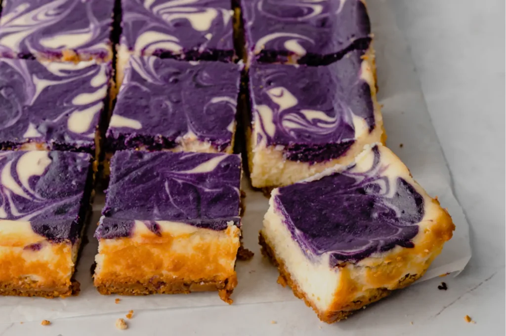 A tray of purple and white swirled cheesecake bars, some cut into squares and one square partially removed.