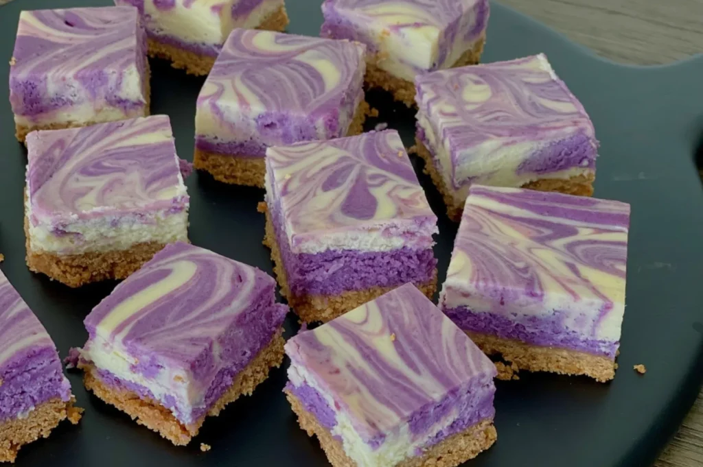 A plate of swirled purple and white cheesecake squares sitting on a dark surface.