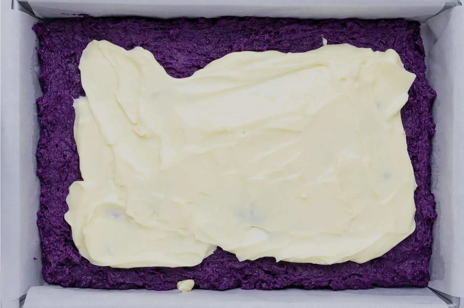 A rectangular dish containing a layer of purple filling topped with a creamy, off-white frosting.