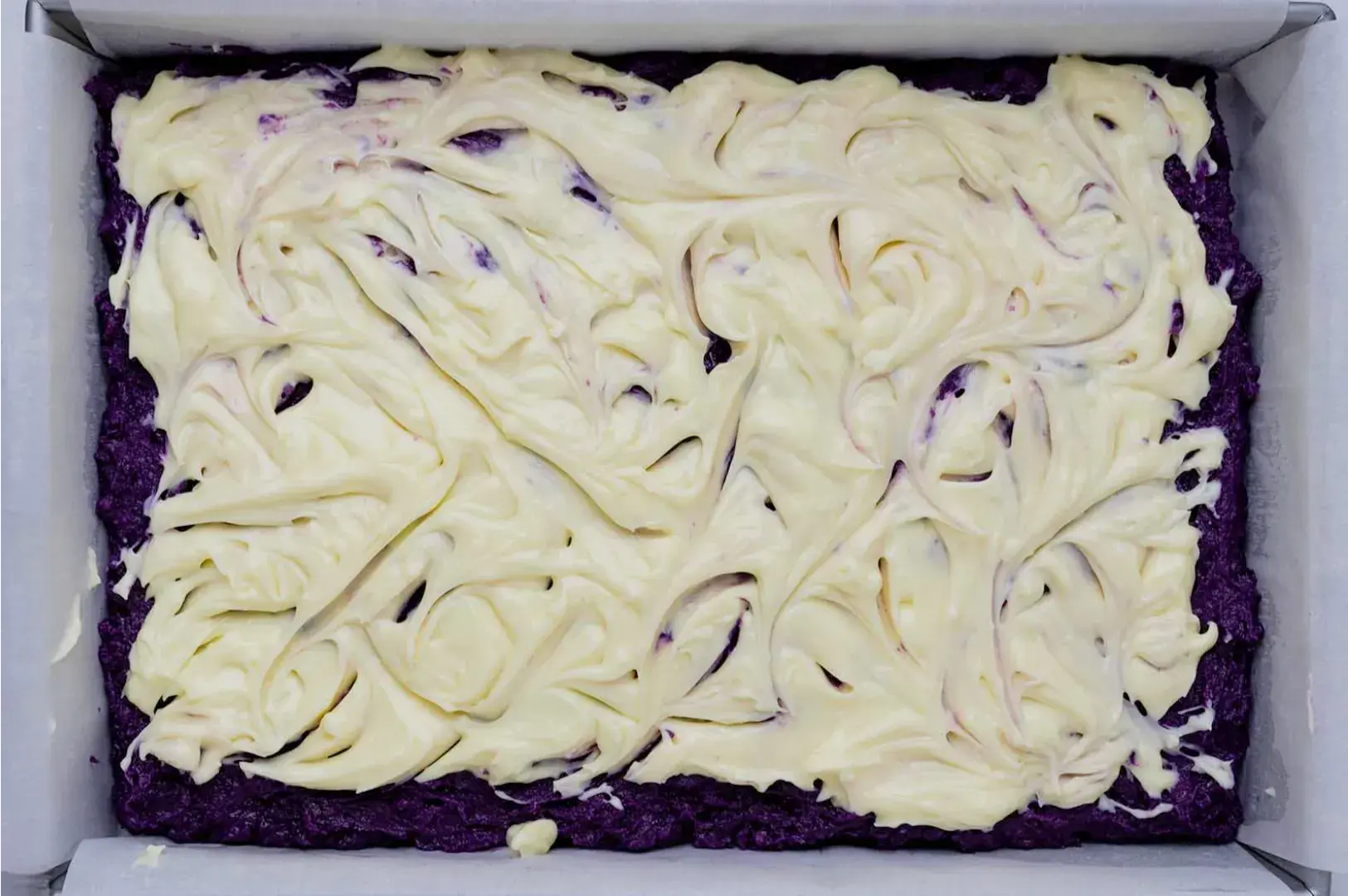 A rectangular dish containing a layer of purple dessert topped with a swirled layer of cream or frosting.