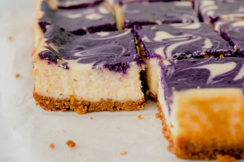 A close-up of slice pieces of purple swirl cheesecake bars on a white surface.