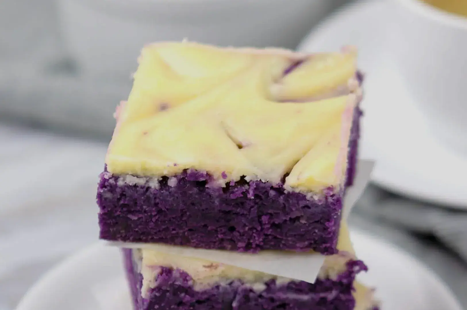 A stack of purple sweet potato brownies with a swirl of cream cheese on top.